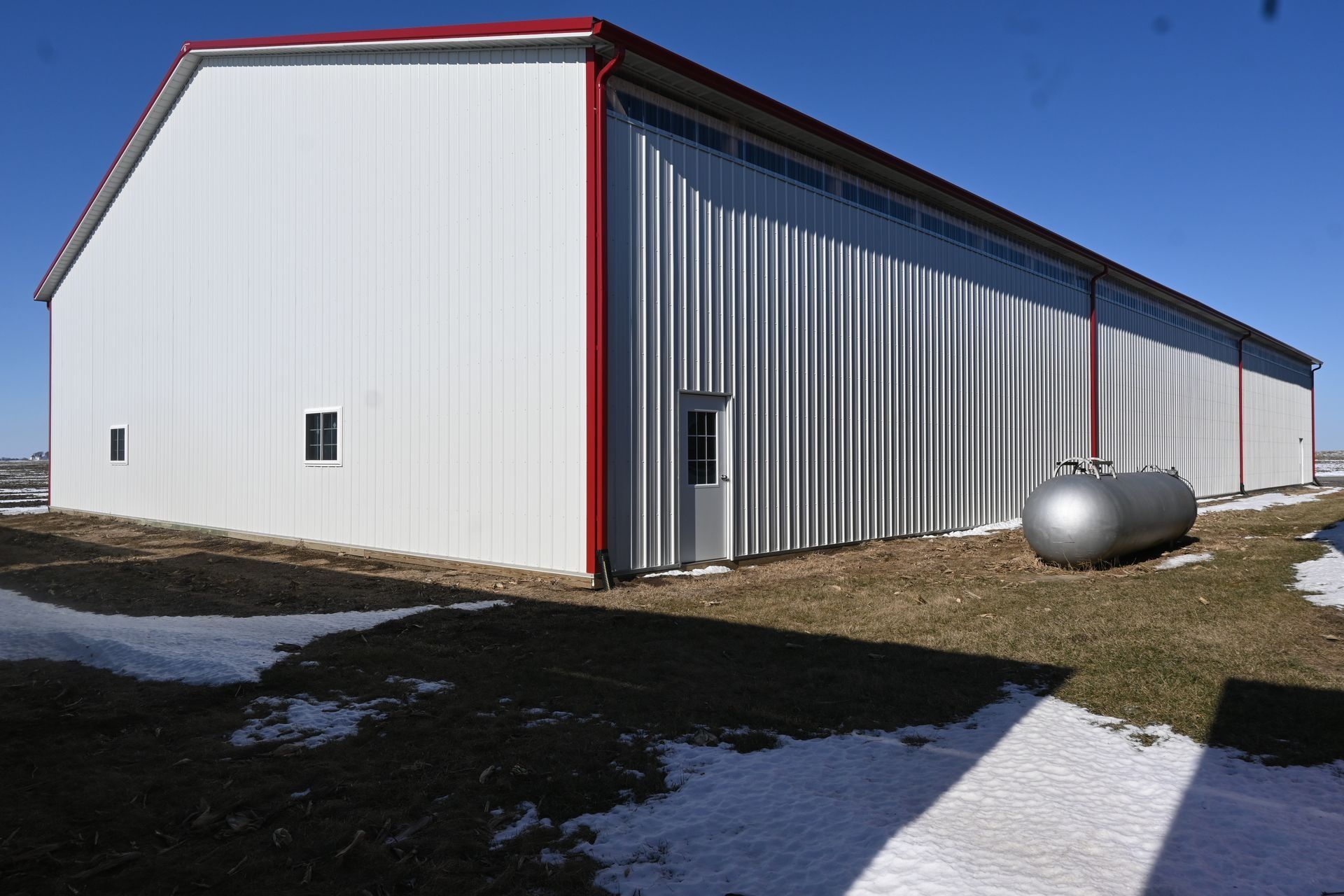 White post-frame building with a red trim line and large overhead door