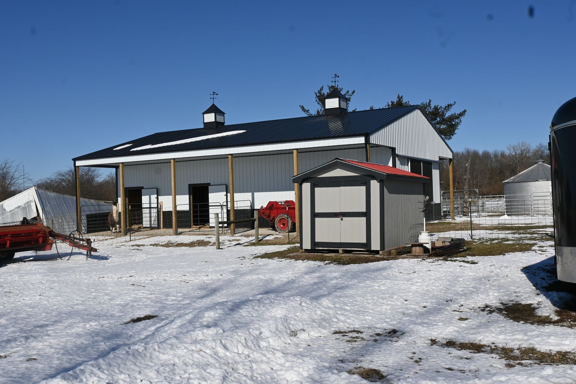 Post-frame building with a covered porch and a cupola, after a snowfall