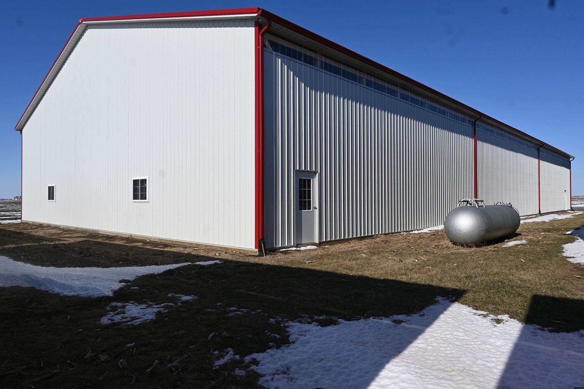 Long white post-frame building with blue wainscot and overhead doors